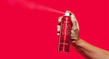 Hand holding Big Dry Shampoo spray can on red background