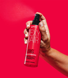 Hand holding Big High Standards spray bottle on red background