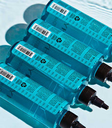 Multiple Healthy SexyHair Gloss N' Glow Rinse bottles stacked on light blue background