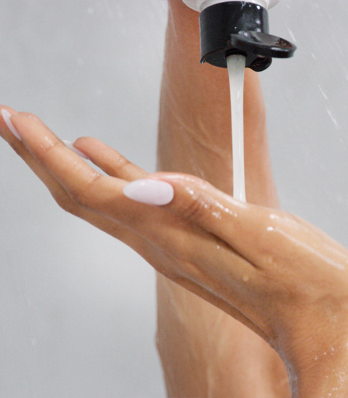 Hand holding shower head dispensing I Want SexyHair Moisture shampoo